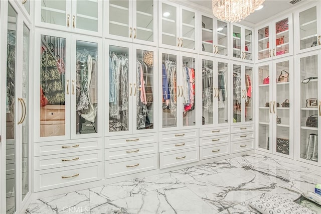 walk in closet with marble finish floor and a chandelier