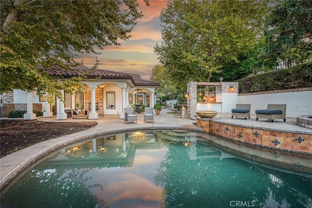 pool at dusk with an outdoor pool, grilling area, a patio, and an outbuilding