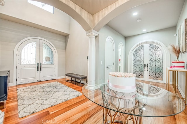 entrance foyer with wood finished floors, baseboards, ornate columns, arched walkways, and french doors