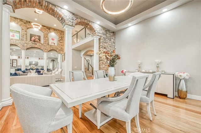 dining room with baseboards, stairs, light wood-style flooring, a towering ceiling, and ornate columns