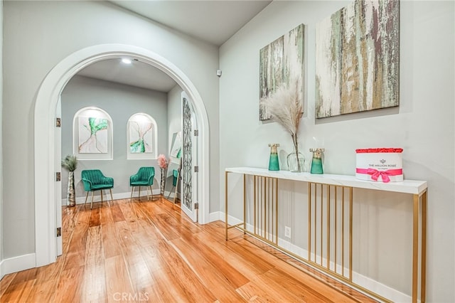 hall featuring baseboards, wood-type flooring, and arched walkways