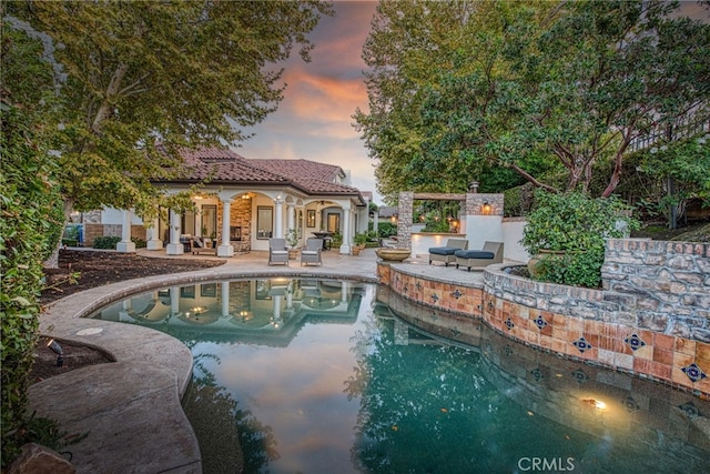 pool at dusk featuring an outbuilding, a storage structure, a patio area, and an outdoor pool