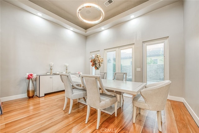 dining space with visible vents, baseboards, a high ceiling, and light wood finished floors