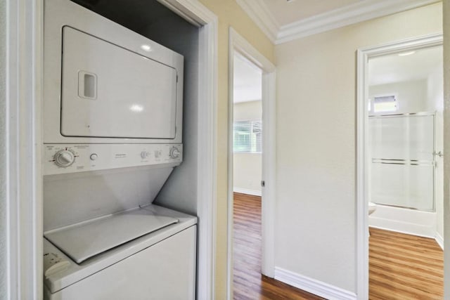 laundry room featuring stacked washer / dryer, baseboards, ornamental molding, laundry area, and wood finished floors