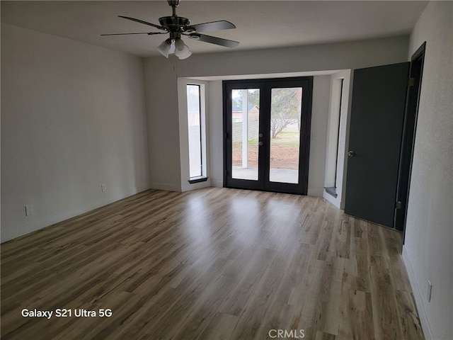 empty room featuring french doors, baseboards, ceiling fan, and wood finished floors