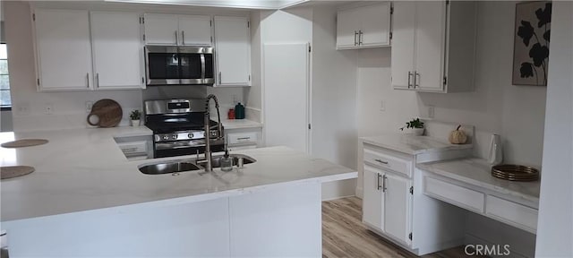 kitchen with light wood finished floors, light stone counters, a peninsula, stainless steel appliances, and a sink