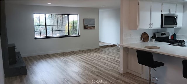 kitchen with baseboards, a breakfast bar, light countertops, appliances with stainless steel finishes, and light wood-style floors