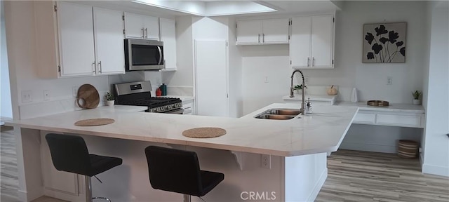 kitchen with a peninsula, a sink, stainless steel appliances, light wood-style floors, and white cabinetry