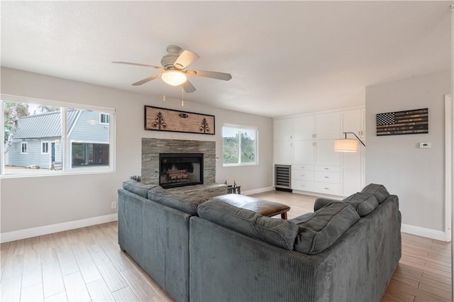 living room featuring a stone fireplace, baseboards, light wood-style floors, and ceiling fan