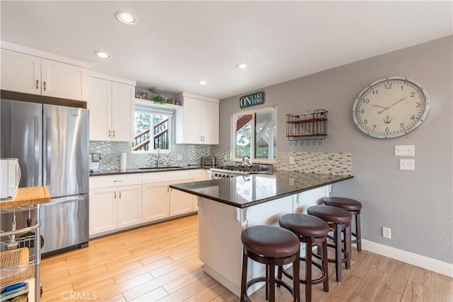 kitchen with a peninsula, freestanding refrigerator, a sink, stove, and white cabinets