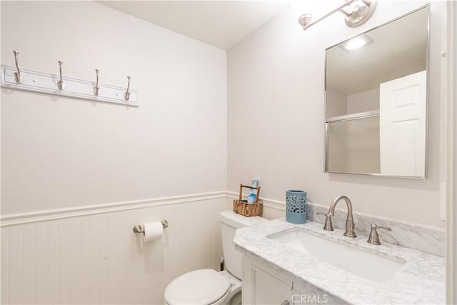 bathroom with vanity, toilet, a shower with door, and wainscoting