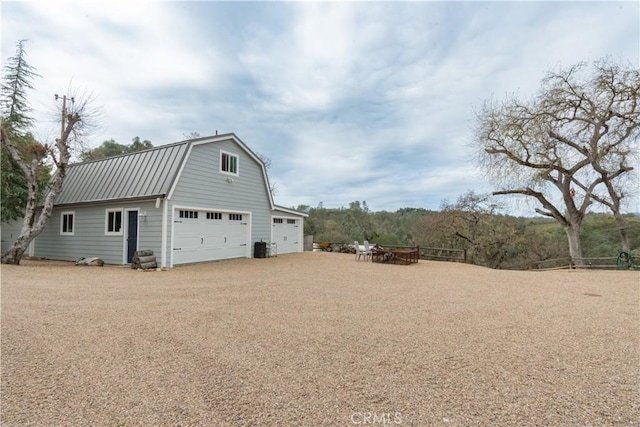 view of property exterior with an outbuilding, a gambrel roof, metal roof, and dirt driveway