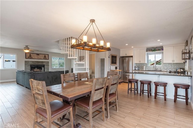 dining area with baseboards, recessed lighting, a fireplace, ceiling fan with notable chandelier, and light wood-type flooring