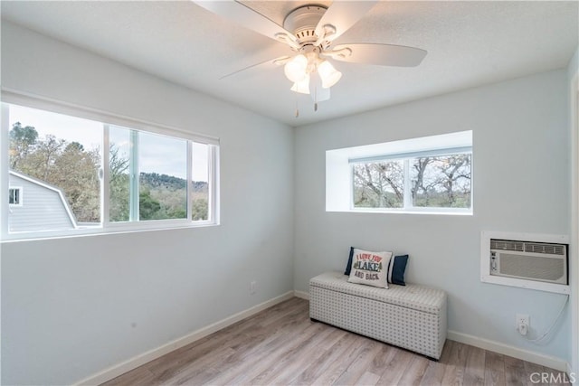 living area with a ceiling fan, light wood-style floors, baseboards, and a wall mounted air conditioner