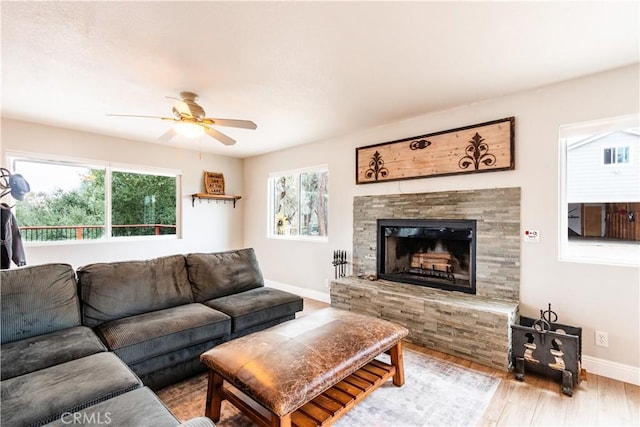 living room with a stone fireplace, baseboards, ceiling fan, and wood finished floors