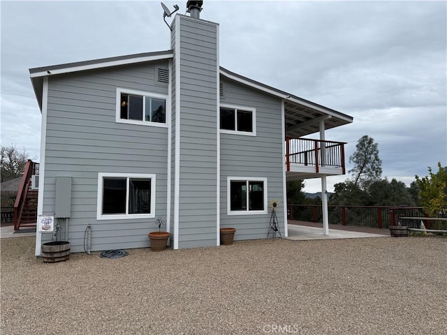 back of house with a balcony, fence, a chimney, stairs, and a patio area