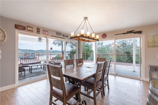 dining area featuring light wood-style flooring, a notable chandelier, baseboards, and a textured ceiling