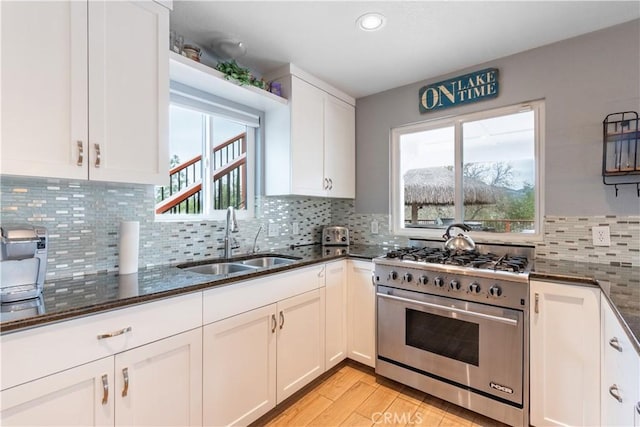 kitchen with a sink, dark stone countertops, white cabinets, and high end stainless steel range