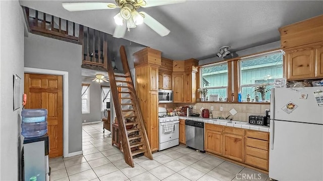 kitchen with a ceiling fan, tile counters, light tile patterned floors, and appliances with stainless steel finishes