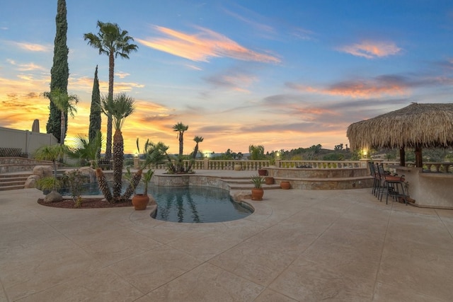 pool at dusk featuring fence, a patio area, an outdoor pool, and outdoor dry bar