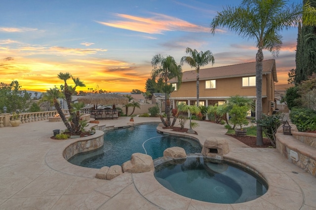 pool at dusk featuring a patio area and a pool with connected hot tub