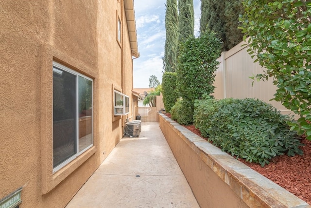 view of side of property with stucco siding, a patio, central AC unit, and fence