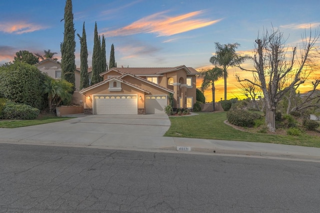 mediterranean / spanish-style home featuring a tile roof, concrete driveway, a lawn, stucco siding, and a garage