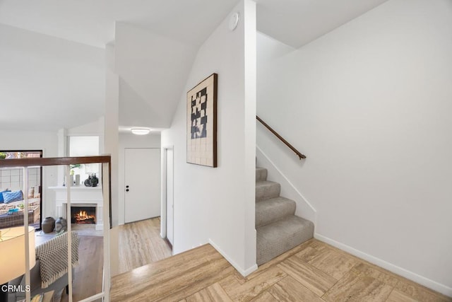 staircase with lofted ceiling, wood finished floors, baseboards, and a warm lit fireplace