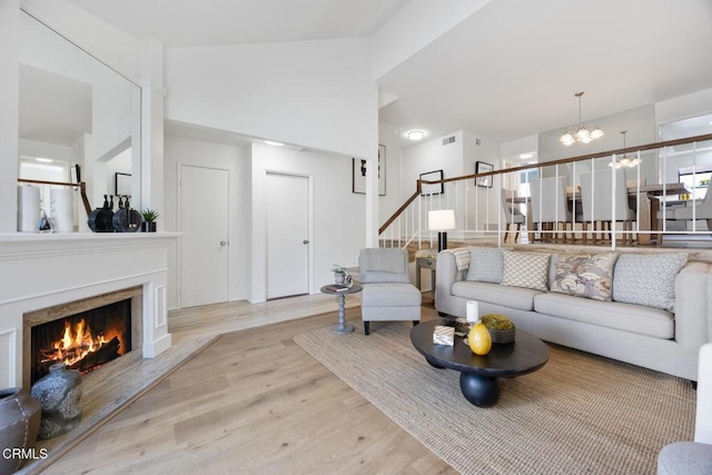 living area featuring visible vents, stairway, a lit fireplace, an inviting chandelier, and wood finished floors