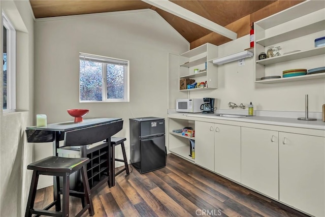 kitchen with white microwave, open shelves, dark wood-type flooring, freestanding refrigerator, and a sink