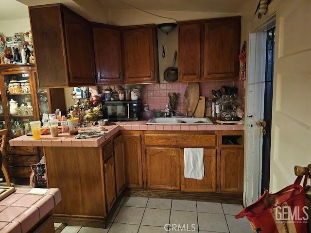 kitchen with tile counters, light tile patterned floors, backsplash, and black microwave