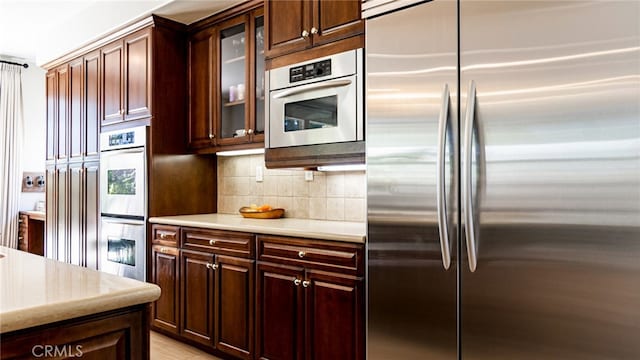 kitchen featuring dark brown cabinets, glass insert cabinets, tasteful backsplash, and appliances with stainless steel finishes