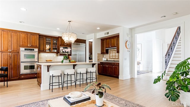 kitchen featuring stainless steel appliances, light countertops, light wood-style floors, a kitchen bar, and a chandelier