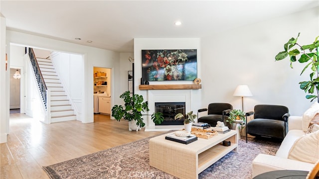 living area featuring stairway, wood finished floors, washer / dryer, recessed lighting, and a glass covered fireplace