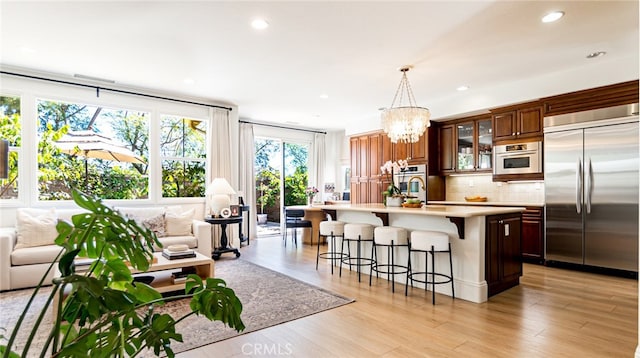 kitchen featuring a breakfast bar area, stainless steel appliances, decorative backsplash, light countertops, and a notable chandelier