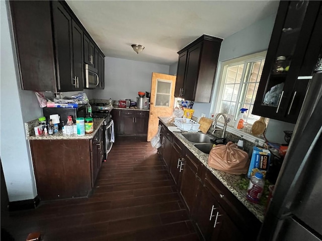 kitchen with dark brown cabinetry, light stone counters, appliances with stainless steel finishes, dark wood-style floors, and a sink