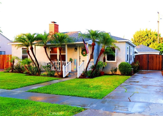 view of front of house with fence, a porch, a front yard, stucco siding, and a chimney