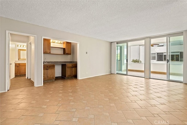 unfurnished living room featuring a textured ceiling, baseboards, and a sink