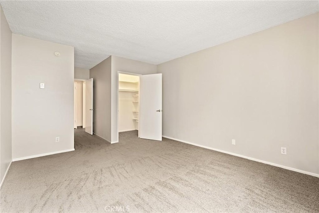 unfurnished bedroom with a walk in closet, baseboards, carpet, a closet, and a textured ceiling