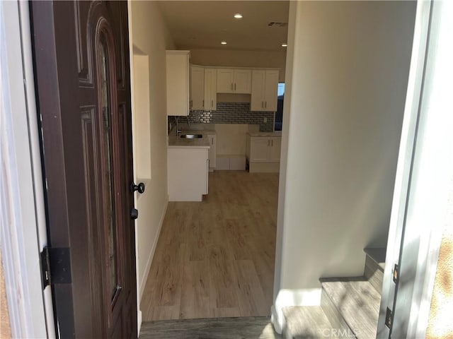 corridor with visible vents, light wood finished floors, and a sink