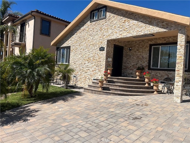 exterior space featuring stucco siding, stone siding, and a patio