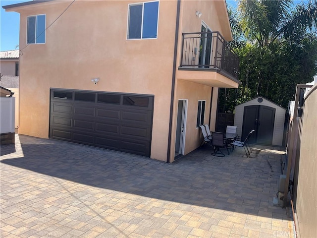 rear view of house with an outbuilding, a balcony, stucco siding, a garage, and a storage shed