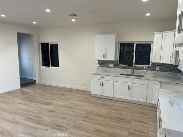 kitchen featuring white cabinetry, backsplash, light wood finished floors, and a sink