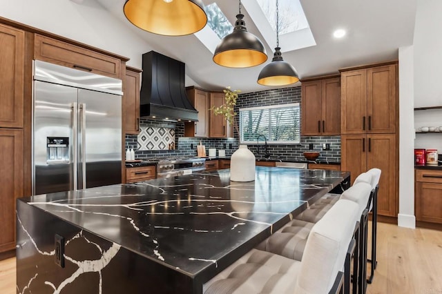 kitchen with premium range hood, a skylight, light wood-style floors, high quality appliances, and brown cabinets