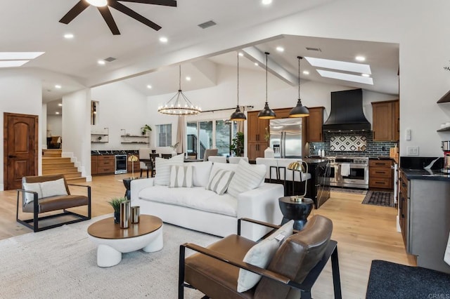 living area with light wood finished floors, visible vents, ceiling fan with notable chandelier, a skylight, and high vaulted ceiling