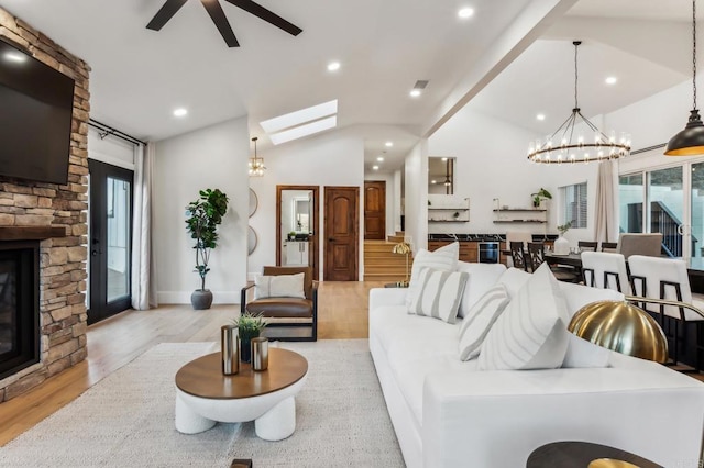 living room featuring lofted ceiling with skylight, ceiling fan with notable chandelier, recessed lighting, light wood-style floors, and a fireplace