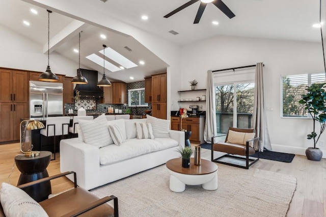 living area with visible vents, light wood-style floors, a skylight, baseboards, and ceiling fan