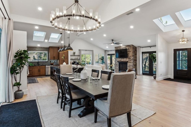 dining room featuring light wood-type flooring, lofted ceiling with skylight, plenty of natural light, and a stone fireplace