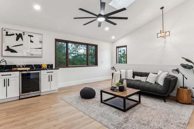 living room featuring beverage cooler, a ceiling fan, light wood finished floors, indoor wet bar, and vaulted ceiling