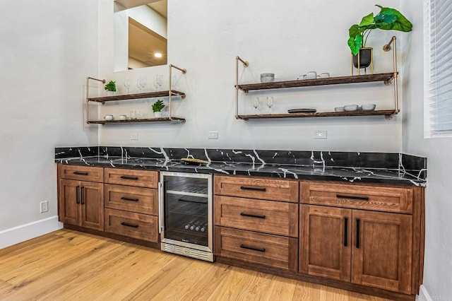 bar featuring wine cooler, light wood-style flooring, a bar, and baseboards